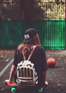 Plastik turuncu penny shortboard şapkalı asfalt üzerinde oturan genç kız