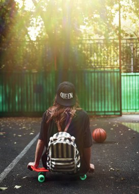 Plastik turuncu penny shortboard şapkalı asfalt üzerinde oturan genç kız