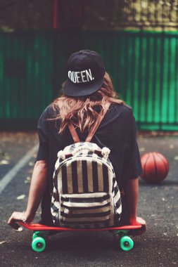 Plastik turuncu penny shortboard şapkalı asfalt üzerinde oturan genç kız