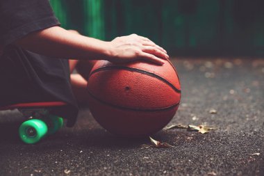 Portre fotoğraf basketbol topu ile plastik turuncu penny shortboard asfalt üzerinde oturan kız 