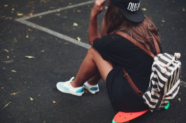 Plastik turuncu penny shortboard şapkalı asfalt üzerinde oturan genç kız