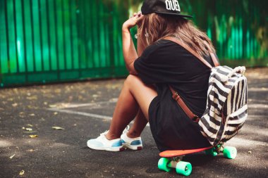 Plastik turuncu penny shortboard şapkalı asfalt üzerinde oturan genç kız