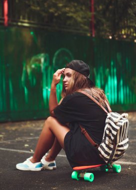 Plastik turuncu penny shortboard şapkalı asfalt üzerinde oturan genç kız