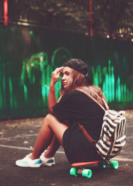 Plastik turuncu penny shortboard şapkalı asfalt üzerinde oturan genç kız