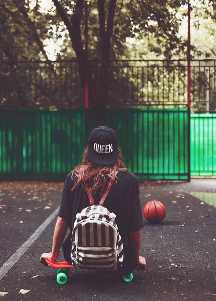 Plastik turuncu penny shortboard şapkalı asfalt üzerinde oturan genç kız