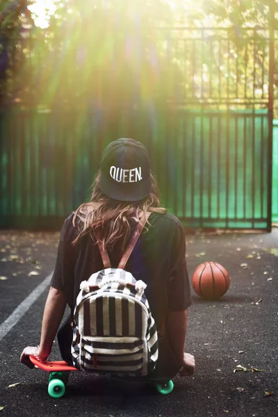 Plastik turuncu penny shortboard şapkalı asfalt üzerinde oturan genç kız