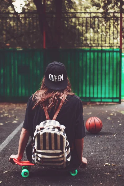 Plastik turuncu penny shortboard şapkalı asfalt üzerinde oturan genç kız