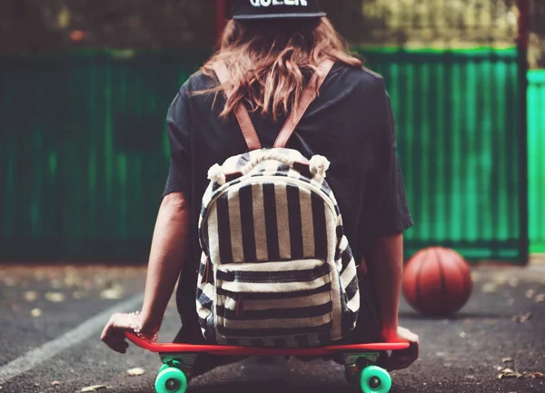 Plastik turuncu penny shortboard şapkalı asfalt üzerinde oturan genç kız