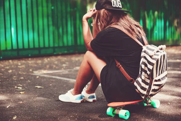 Plastik turuncu penny shortboard şapkalı asfalt üzerinde oturan genç kız