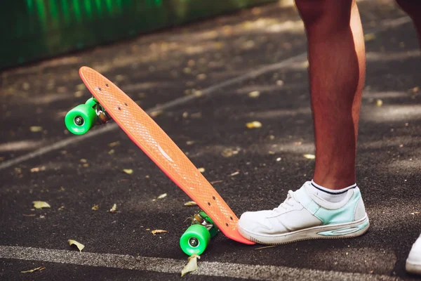 Close up of feet of man sneakers rides on orange penny skateboard on asphalt