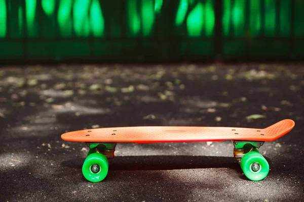 Εσωτερικη Πορτοκαλί Δεκάρα Skateboard Στην Άσφαλτο Πίσω Από Πράσινο Τοίχο — Φωτογραφία Αρχείου
