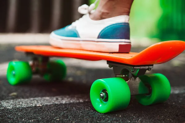 Close up of feet of girl sneakers rides on orange penny skateboard on asphalt