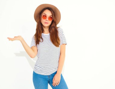 Bir şey elini rahat yaz giysileri üzerinde kahverengi şapka ile doğal makyaj beyaz arka plan üzerinde izole tutan genç şık kız modeli portresi. İçinde güneş gözlüğü