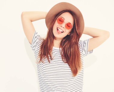 Genç şık gülen kız modeli rahat yaz giysileri ile doğal makyaj beyaz arka plan üzerinde izole kahverengi şapkalı portresi. Dilini gösterilen