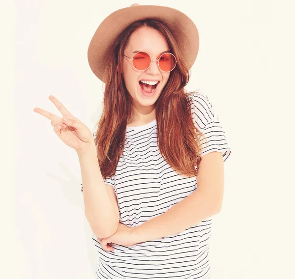 Genç şık gülen kız modeli rahat yaz giysileri ile doğal makyaj beyaz arka plan üzerinde izole kahverengi şapkalı portresi. Barış işareti gösterilen