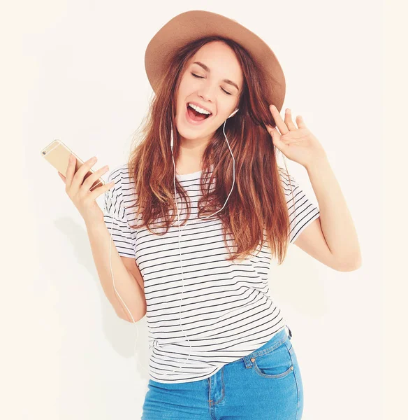 güzel gülen esmer kadın kız rahat hipster yaz giysileri kahverengi şapka dinleme müzik kulaklık ile smartphone içinde hiç makyaj ile