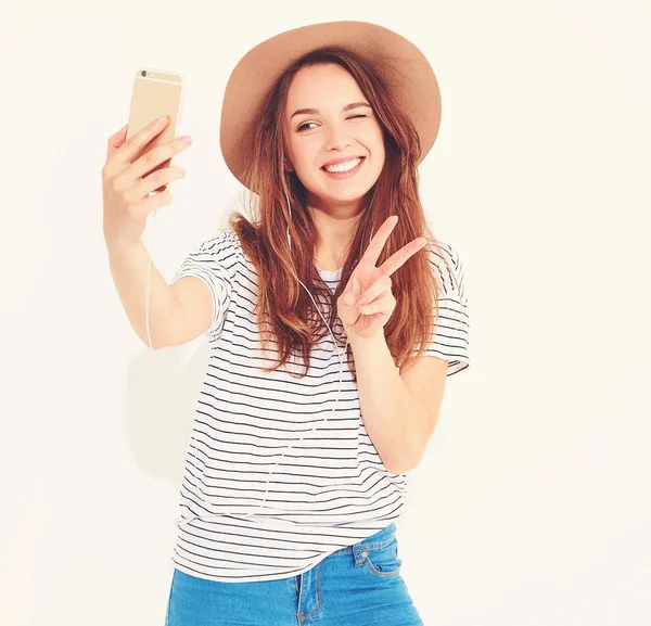 Yaz hipster giysileri beyaz arka plan üzerinde izole bir selfie alarak güzel bir kız portresi. Göz kırpıyor ve barış işareti gösterilen