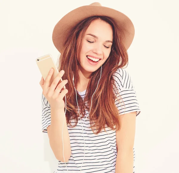 güzel gülen esmer kadın kız rahat hipster yaz giysileri kahverengi şapka dinleme müzik kulaklık ile smartphone içinde hiç makyaj ile