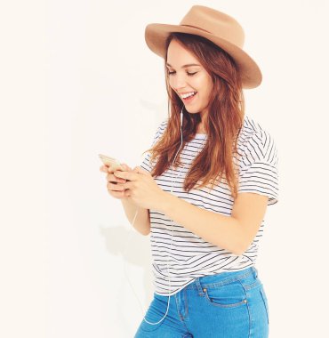 güzel gülen esmer kadın kız rahat hipster yaz giysileri kahverengi şapka dinleme müzik kulaklık ile smartphone içinde hiç makyaj ile