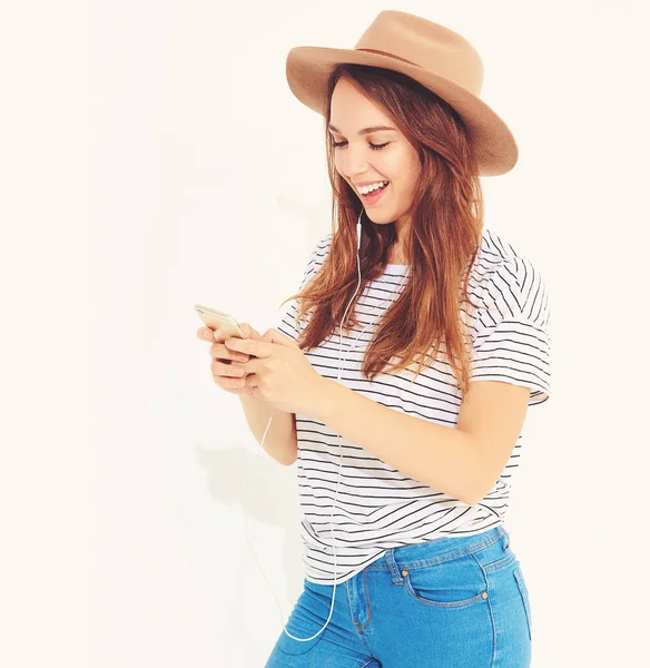 güzel gülen esmer kadın kız rahat hipster yaz giysileri kahverengi şapka dinleme müzik kulaklık ile smartphone içinde hiç makyaj ile