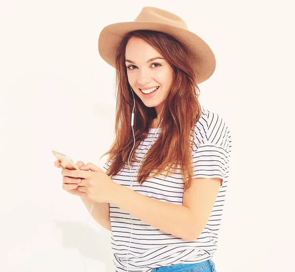 güzel gülen esmer kadın kız rahat hipster yaz giysileri kahverengi şapka dinleme müzik kulaklık ile smartphone içinde hiç makyaj ile