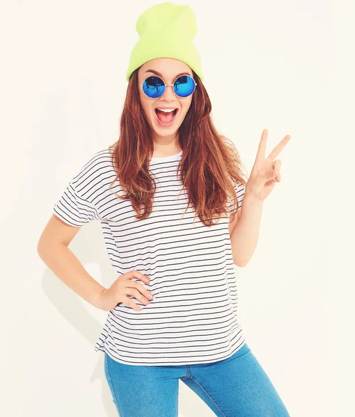 Portre rahat yaz aylarında genç şık kız modelinin üzerinde beyaz izole sarı bere şapka elbise. Barış işareti gösterilen