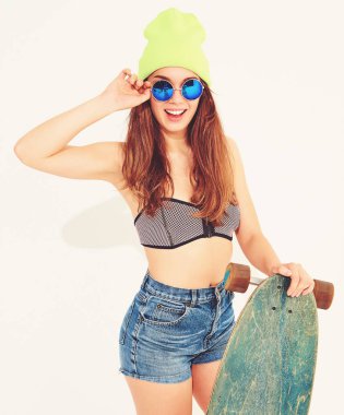 Genç şık gülümseyen kız modeli rahat yaz mayo giysiler ve sarı beanie longboard resepsiyon ile poz portresi. Beyaz izole