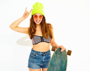 Genç şık gülümseyen kız modeli rahat yaz mayo giysiler ve sarı beanie rock'n roll işaret gösteren longboard resepsiyon ile poz. Beyaz izole