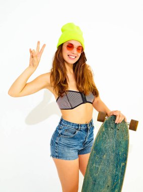Genç şık gülümseyen kız modeli rahat yaz mayo giysiler ve sarı beanie. barış işareti gösterilen longboard resepsiyon ile poz. Beyaz izole