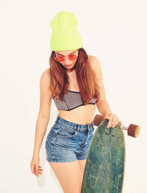 Genç şık gülümseyen kız modeli rahat yaz mayo giysiler ve sarı beanie longboard resepsiyon ile poz portresi. Beyaz izole