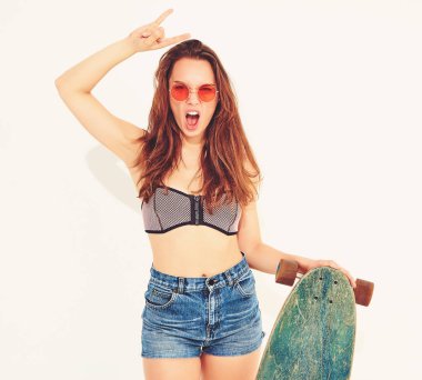 genç şık gülümseyen kız modeli rahat yaz mayo giysileri longboard resepsiyon ile poz. Rock'n roll işaret gösteren