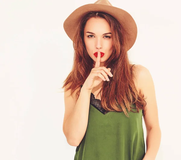 Genç şık kız modeli rahat yaz yeşil giysiler ve sessizlik jest parmağınızla gösterilen Kırmızı dudaklar ile kahverengi şapka izole 