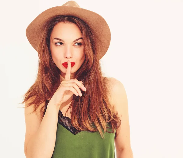 Genç şık kız modeli rahat yaz yeşil giysiler ve sessizlik jest parmağınızla gösterilen Kırmızı dudaklar ile kahverengi şapka izole 