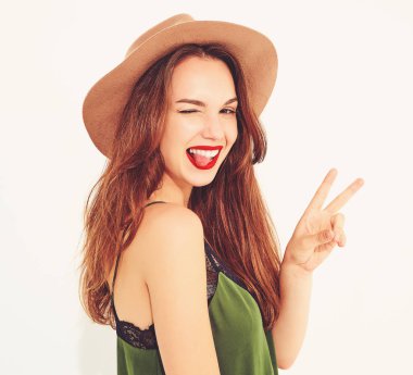 Genç şık kız modeli rahat yaz yeşil giysiler ve kırmızı dudaklar ile kahverengi şapka. Göz kırpıyor ve dilini gösteren