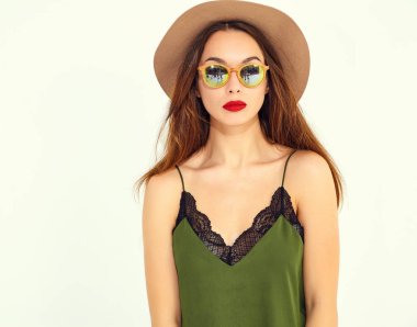 Genç şık kız modeli rahat yaz yeşil giysiler ve kırmızı dudaklı beyaz duvara yakın poz, kahverengi şapka