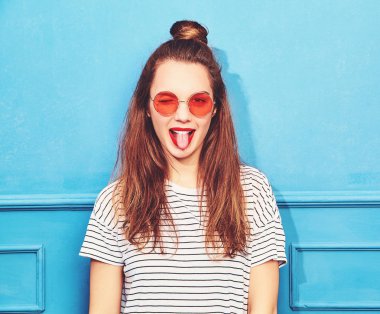 Gündelik yaz kıyafetleri kırmızı dudaklar, mavi duvara yakın poz ile genç şık kız modeli. Göz kırpıyor ve dilini gösteren