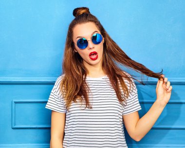 Gündelik yaz kıyafetleri kırmızı dudaklar, mavi duvara yakın poz ile genç şık kız modeli. Saçları ile oynamak