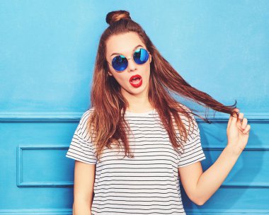 Gündelik yaz kıyafetleri kırmızı dudaklar, mavi duvara yakın poz ile genç şık kız modeli. Saçları ile oynamak