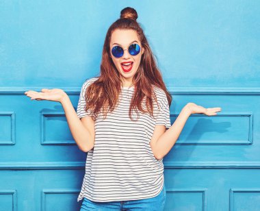 Karşılaştırma kavramı. Mavi duvara yakın poz genç esmer kadın rahat yaz hipster giysileri bir ürün, benzer seçimi için düz iki elle görüntülemek