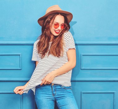 Gündelik yaz kıyafetleri ve kahverengi şapka kırmızı dudaklar, mavi duvara yakın poz ile genç şık kız model