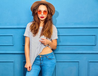 Gündelik yaz kıyafetleri ve kahverengi şapka kırmızı dudaklar, mavi duvara yakın poz ile genç şık kız model