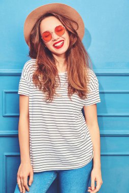 Gündelik yaz kıyafetleri ve kahverengi şapka kırmızı dudaklar, mavi duvara yakın poz ile genç şık kız model