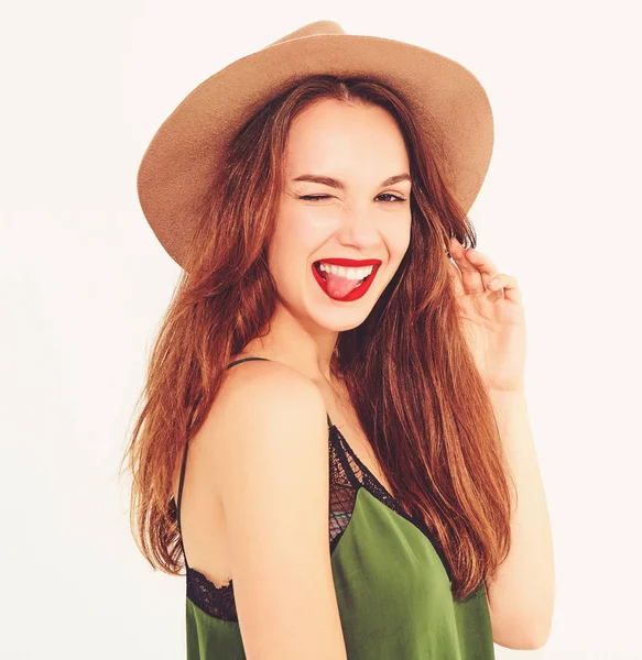 Genç şık kız modeli rahat yaz yeşil giysiler ve kırmızı dudaklar ile kahverengi şapka. Göz kırpıyor ve dilini gösteren