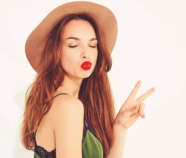 Genç şık kız modeli rahat yaz yeşil giysiler ve kırmızı dudaklar ile kahverengi şapka. Barış işareti gösterilen ve öpücük vererek