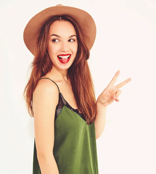 Genç şık kız modeli rahat yaz yeşil giysiler ve barış işareti ve dilini gösteren kırmızı dudaklar ile kahverengi şapka