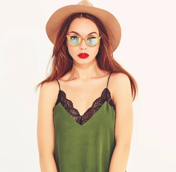 Genç şık kız modeli rahat yaz yeşil giysiler ve kırmızı dudaklı beyaz duvara yakın poz, kahverengi şapka