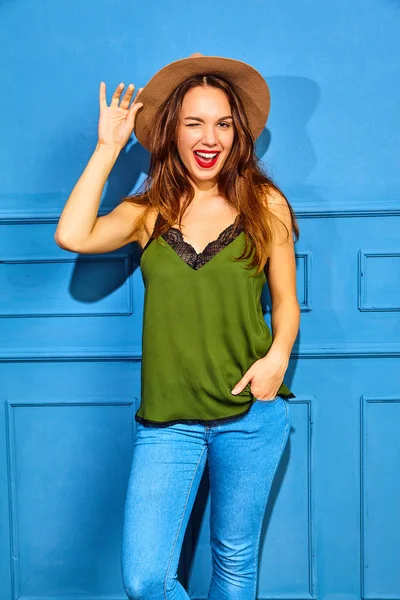 カジュアルな夏緑服と赤い唇 青い壁に近いポーズで茶色の帽子でスタイリッシュな少女モデルの まばたき — ストック写真