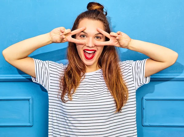 Gündelik yaz kıyafetleri kırmızı dudaklar, mavi duvara yakın poz ile genç şık kız modeli. Çığlık ve barış işareti gösterilen