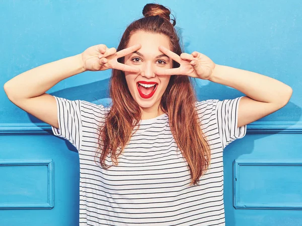 Gündelik yaz kıyafetleri kırmızı dudaklar, mavi duvara yakın poz ile genç şık kız modeli. Çığlık ve barış işareti gösterilen