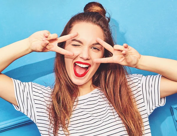 Gündelik yaz kıyafetleri kırmızı dudaklar, mavi duvara yakın poz ile genç şık kız modeli. Göz kırpıyor